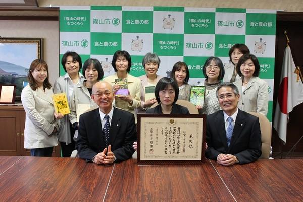 市長と篠山ストリーテリングの会代表の女性が表彰状を持ち前に座り、会員の皆さんが本を手にもって後ろに立っている集合写真